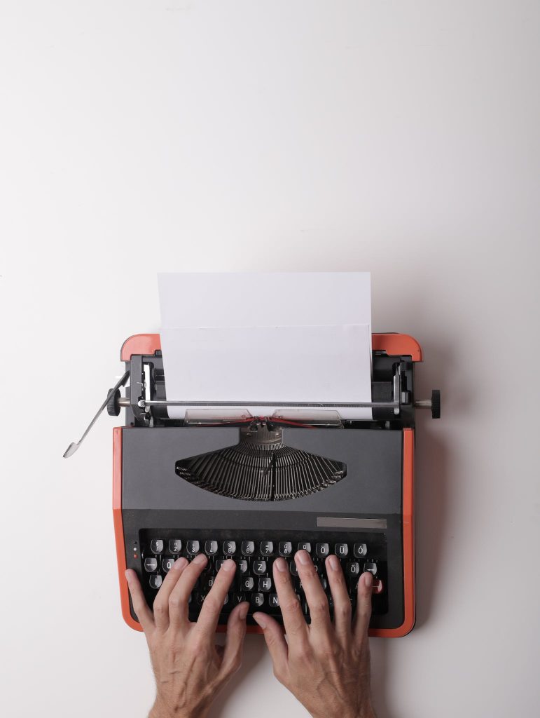 From above crop person using vintage black and red typewriter with white blank sheet of paper against white background